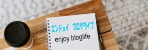 机の上のコーヒーカップと運ジョイブログライフと書かれたノートが置いてある画像