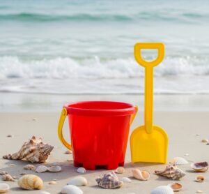 海の波打ち際で砂遊び用のプラスチックのスコップをとバケツが置いてある画像