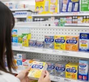 棚には様々な鎮咳去痰薬やのどケア商品が並んでおり、その中の浅田飴せきどめを手に持っている画像