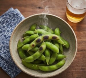 製のテーブルの上に、茹で上がったばかりでまだ湯気の立つ丹波黒枝豆が、素朴な陶器の器に盛られている画像