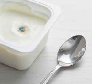 清潔な白いテーブルの上に、食べかけのヨーグルトが入った容器にカビらしいものが出来た様子