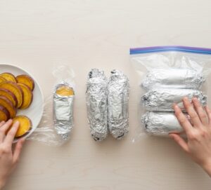 完全に冷ました一口サイズの焼き芋の切り身、ぴったりと巻かれたラップ、アルミホイル、そして空気を抜いた状態の冷凍用ジッパー付き保存袋。